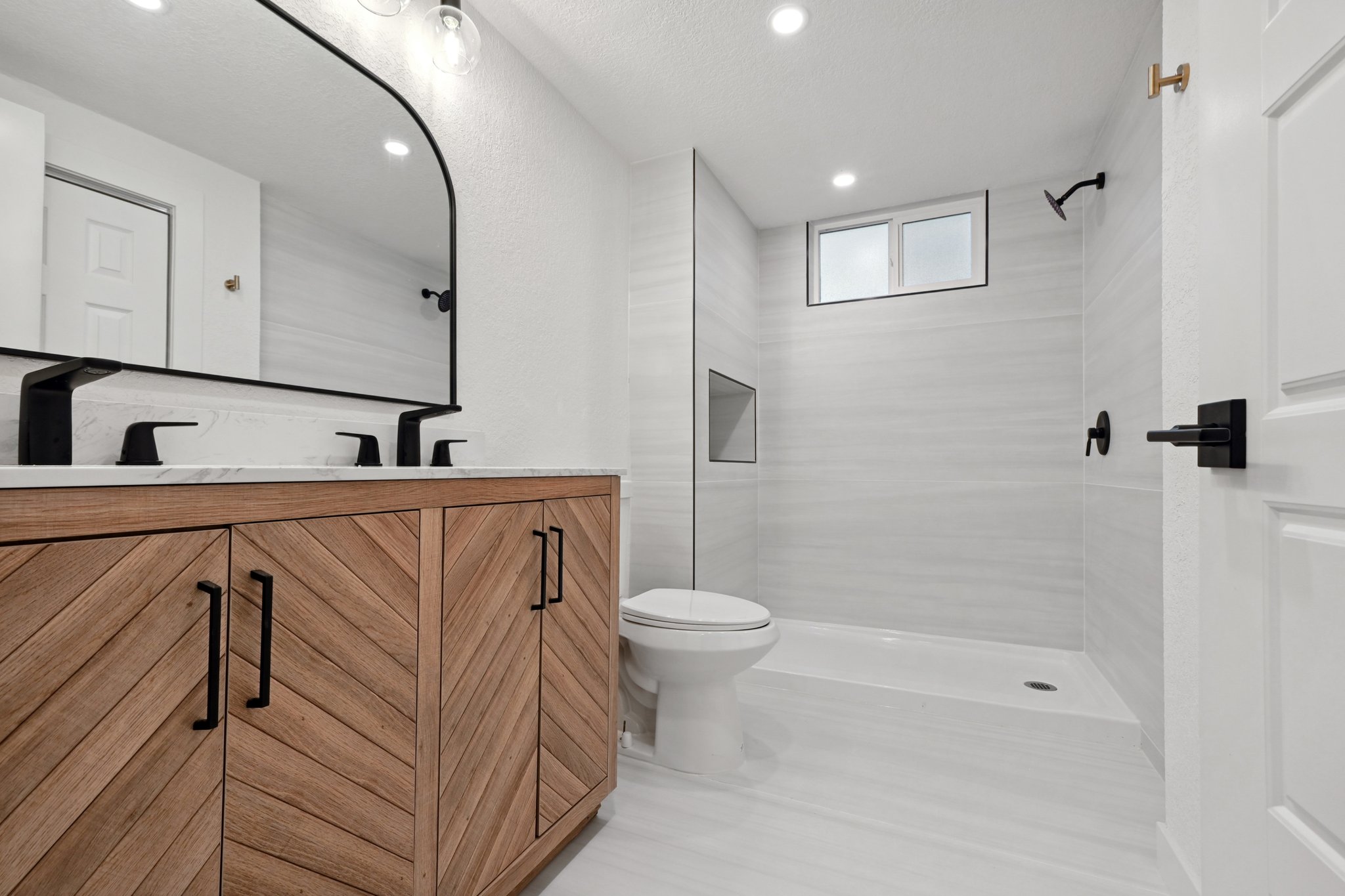 Bathroom remodel in Lakewood with warm wood vanity, large format tile shower and matte black fixtures